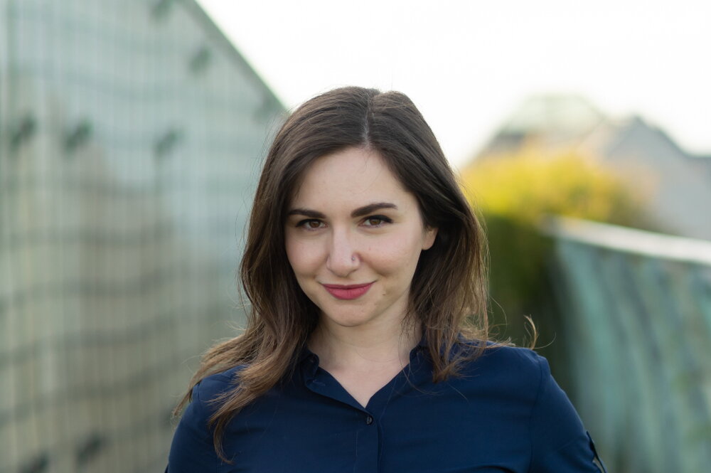 A woman with brown hair wearing a dark blue button-up shirt is smiling at the camera.