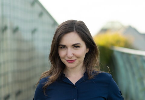 A woman with brown hair wearing a dark blue button-up shirt is smiling at the camera.